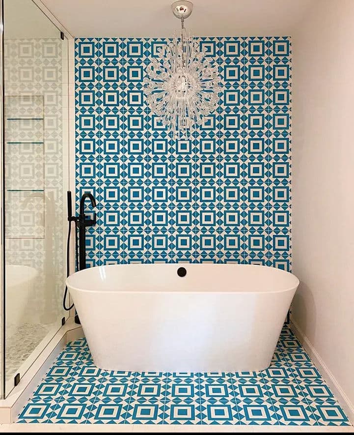 Modern bathroom with a freestanding tub, blue patterned tile wall, and stylish chandelier.