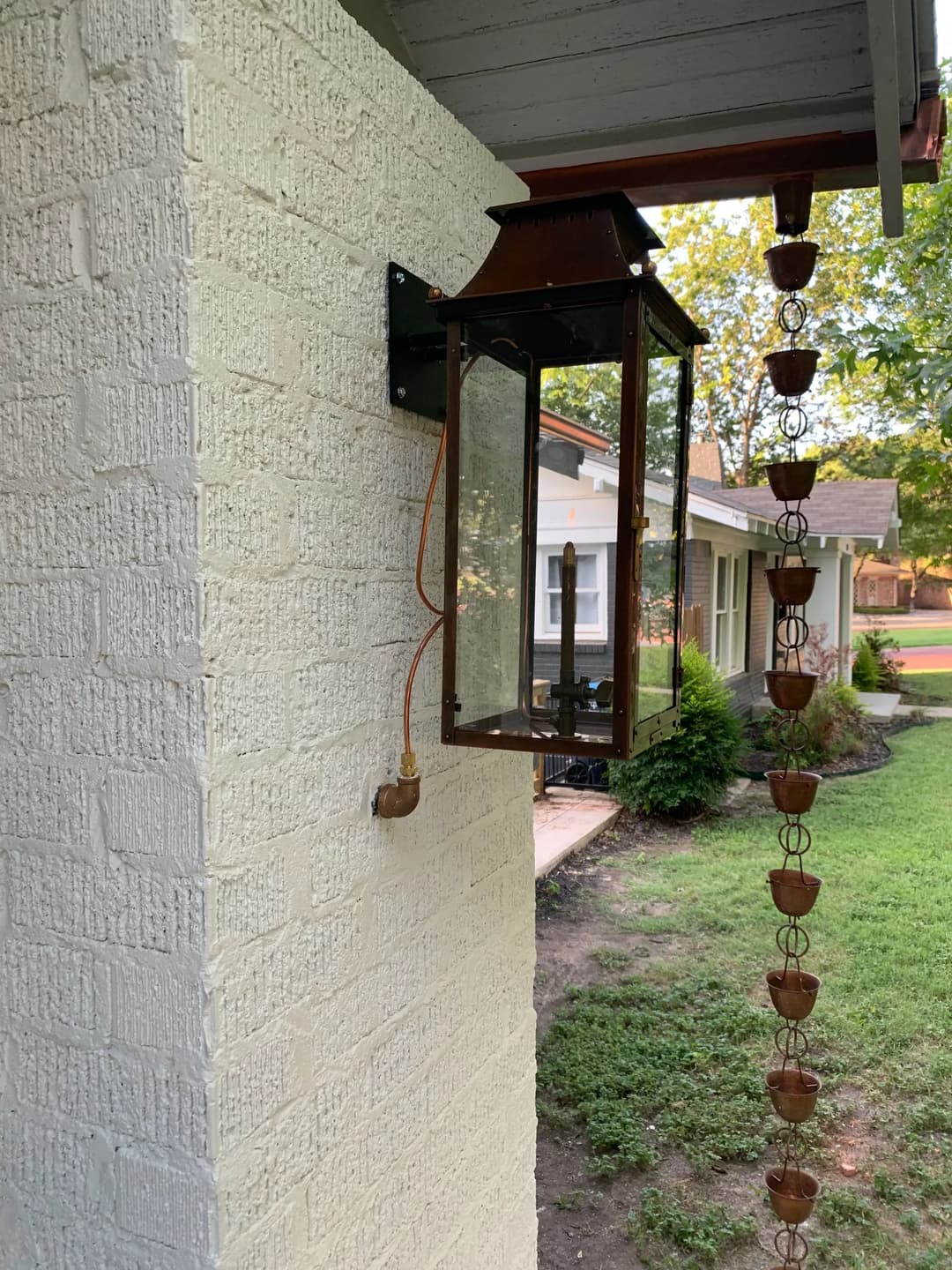 Rustic wall lantern mounted on a home, with a copper rain chain nearby.