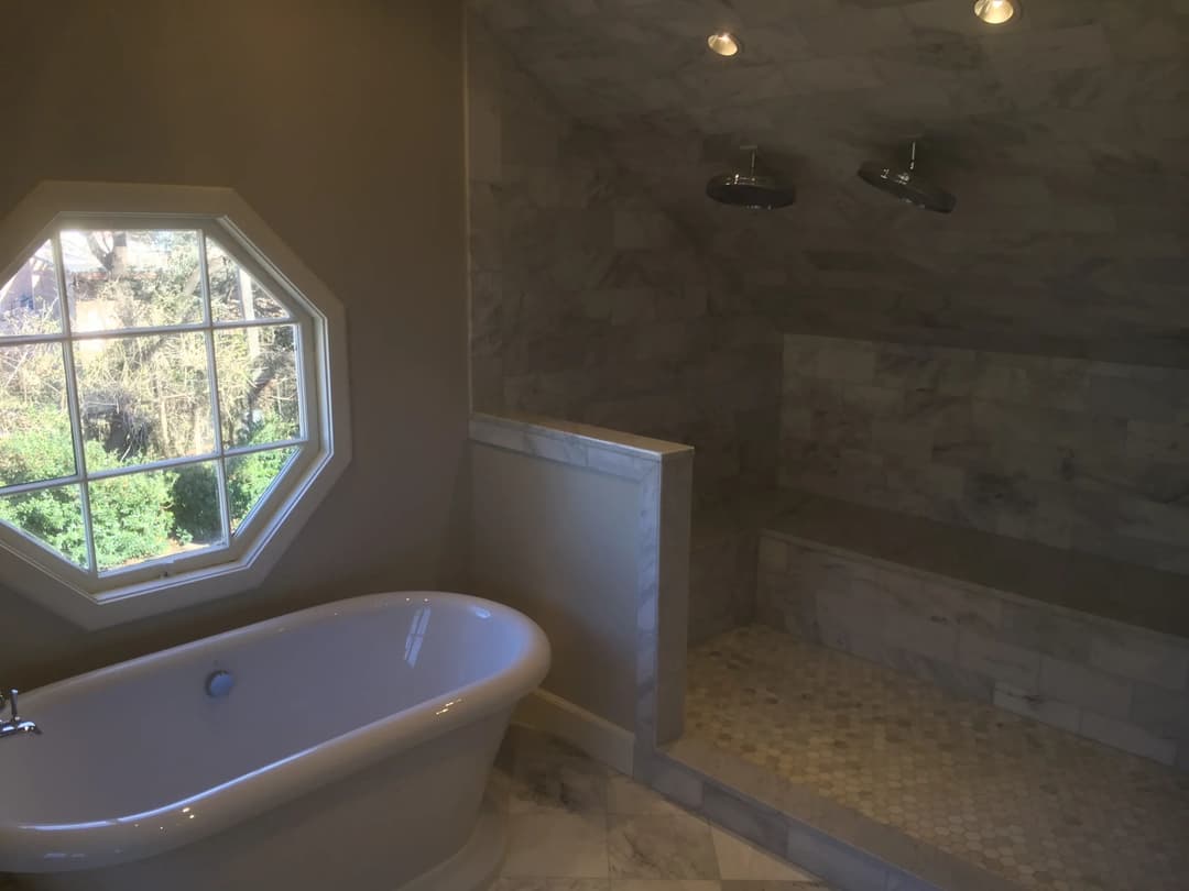 Modern bathroom with octagonal window, freestanding tub, and marble shower.