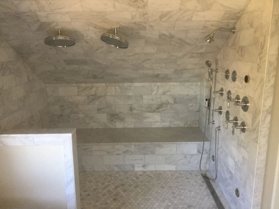 Luxurious marble shower with dual rainfall showerheads and multiple body sprays.