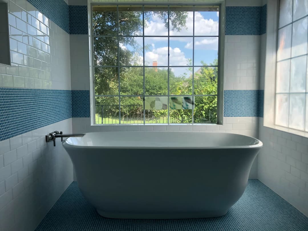 Modern bathroom featuring a freestanding bathtub and large windows with a view of greenery.