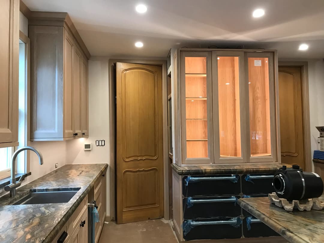 Modern kitchen interior featuring wooden cabinets, granite countertops, and a glass-fronted display cabinet.