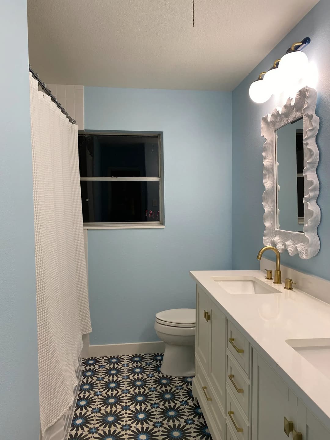 Modern bathroom featuring blue walls, white fixtures, and patterned floor tiles. Bright and inviting.