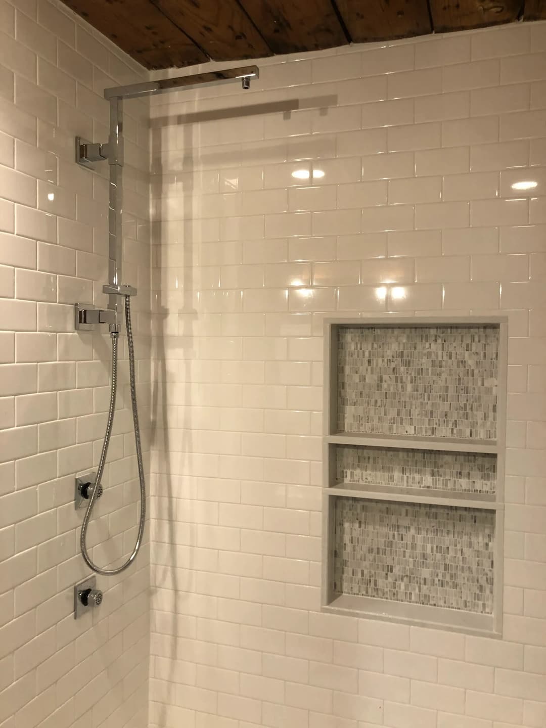 Modern shower design with a sleek showerhead and built-in tile shelf in a white tiled bathroom.