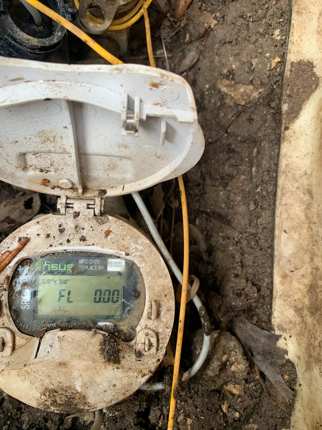 Water meter displaying readings in a muddy, outdoor setting.