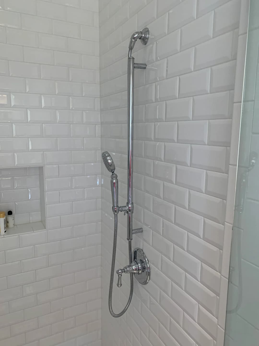 Modern shower fixture with handheld showerhead in a tiled bathroom.