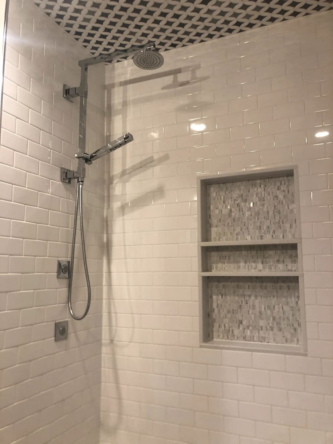 Modern shower with overhead and handheld fixtures, featuring white tile and a geometric accent wall.