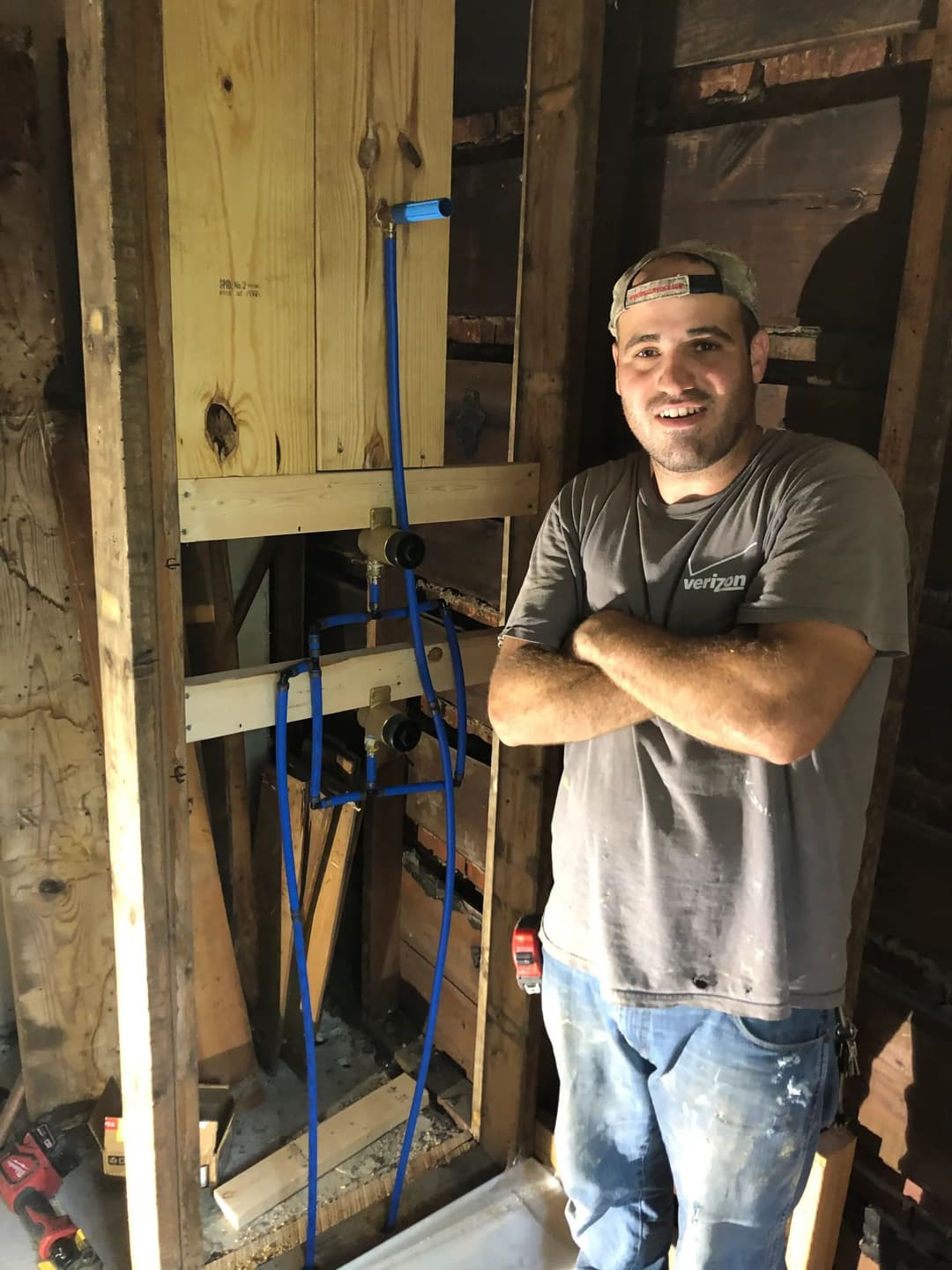 Plumber standing by framed wall with blue water pipes during home renovation.