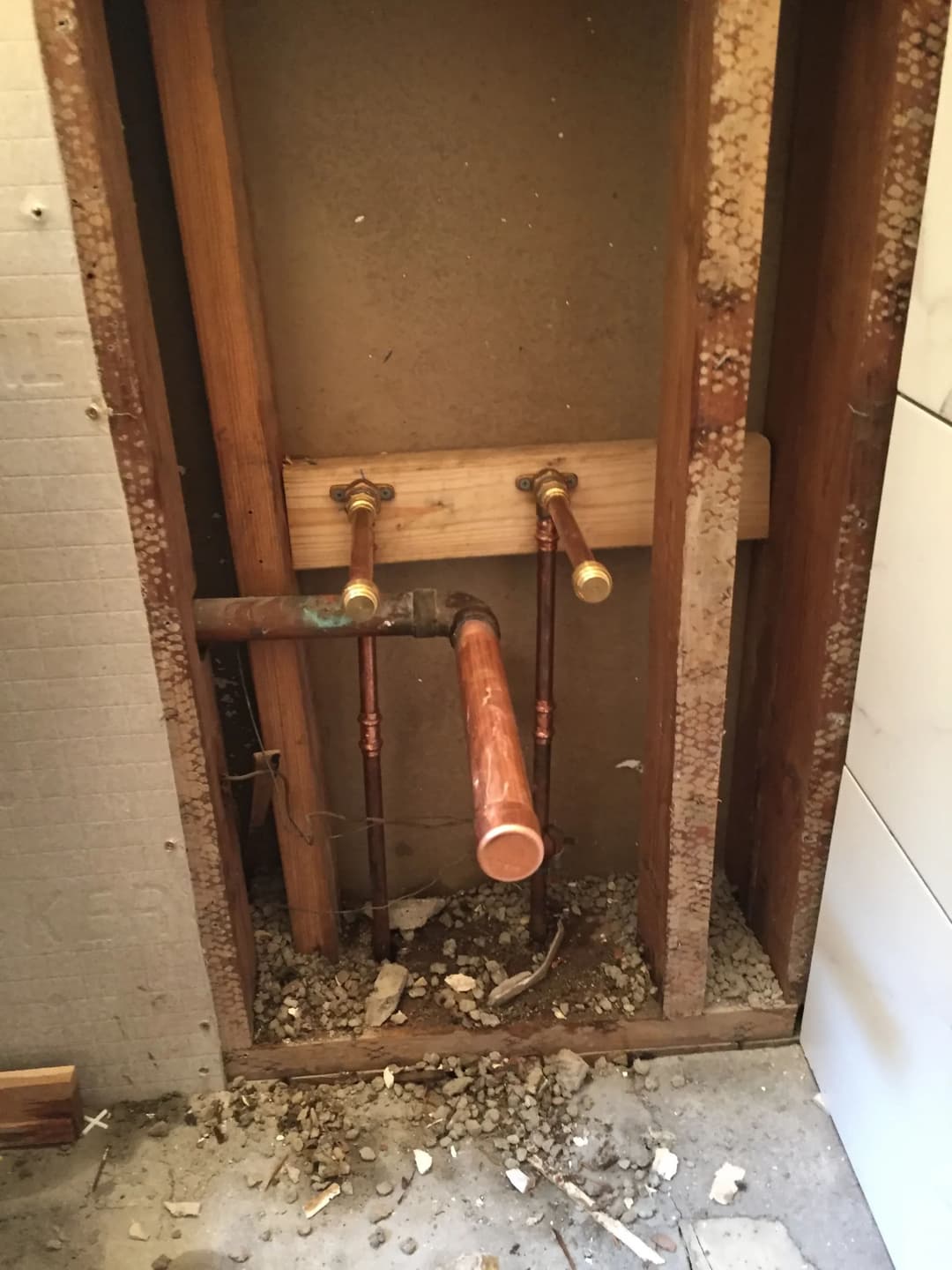 Exposed plumbing pipes in a bathroom renovation, showing copper and brass fixtures.