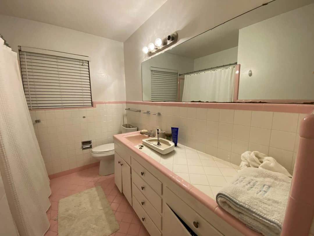 Modern bathroom with pink accents, white cabinetry, and a shower curtain.