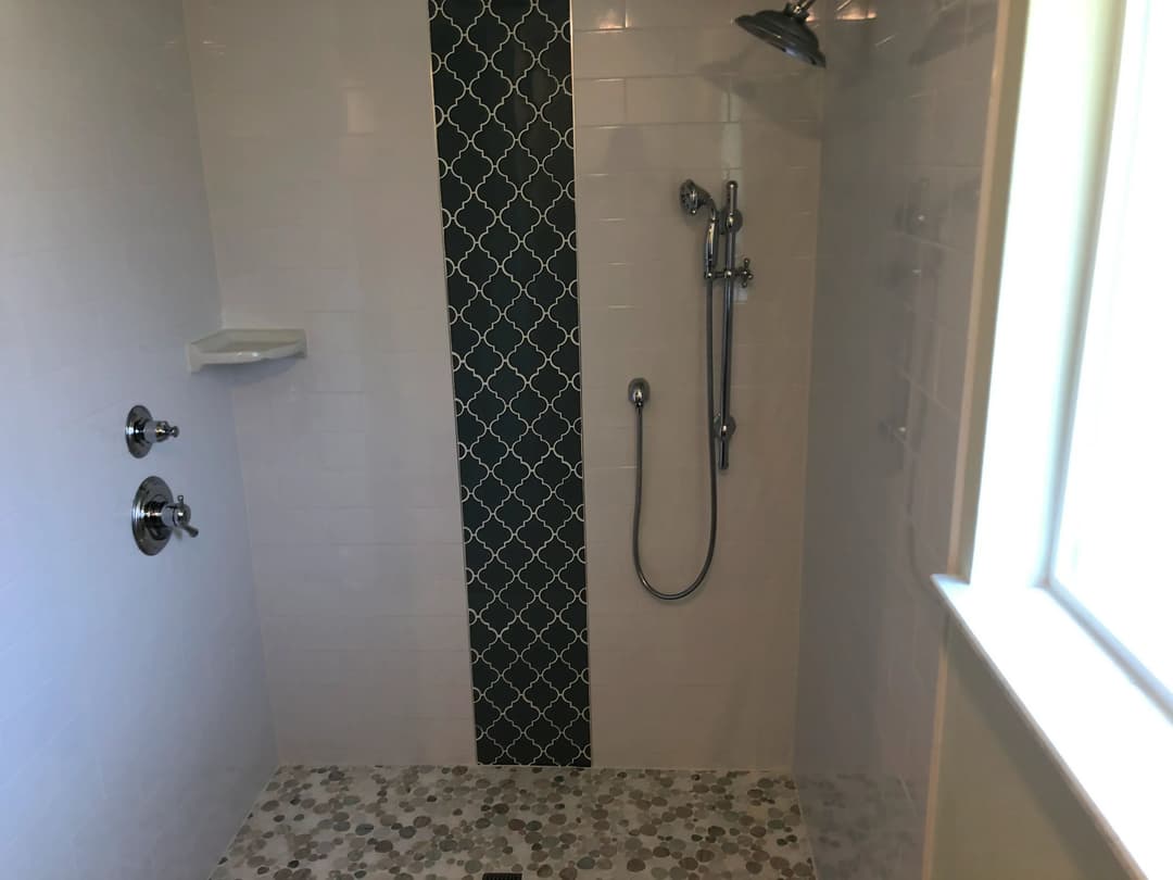 Modern shower with decorative tile accent, handheld showerhead, and pebble floor.