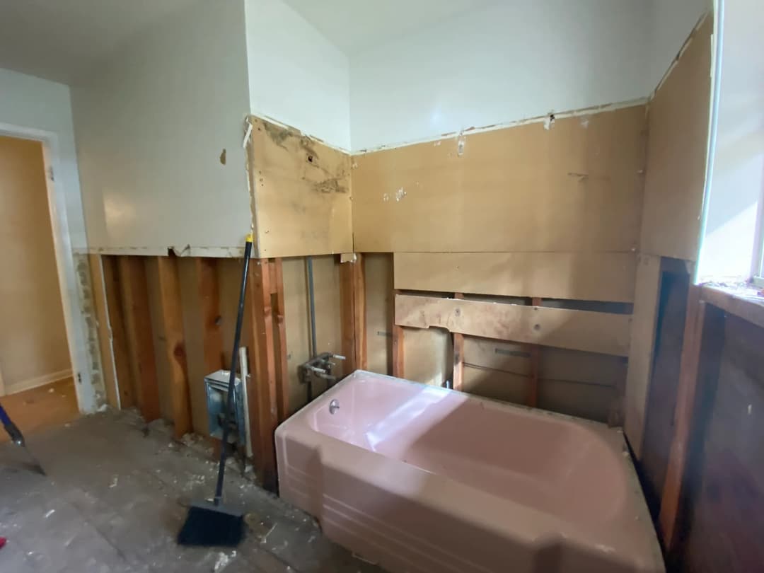 Renovation progress of a bathroom with exposed walls and a pink tub in a remodel.