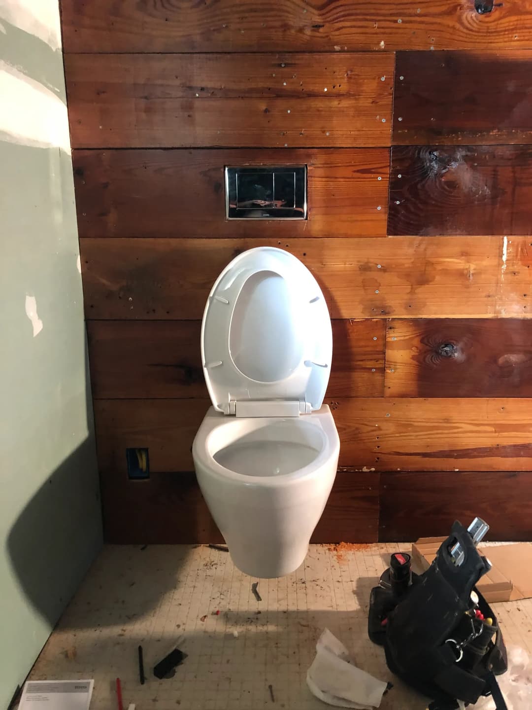 Modern white toilet installed against a rustic wooden wall in a renovation setting.