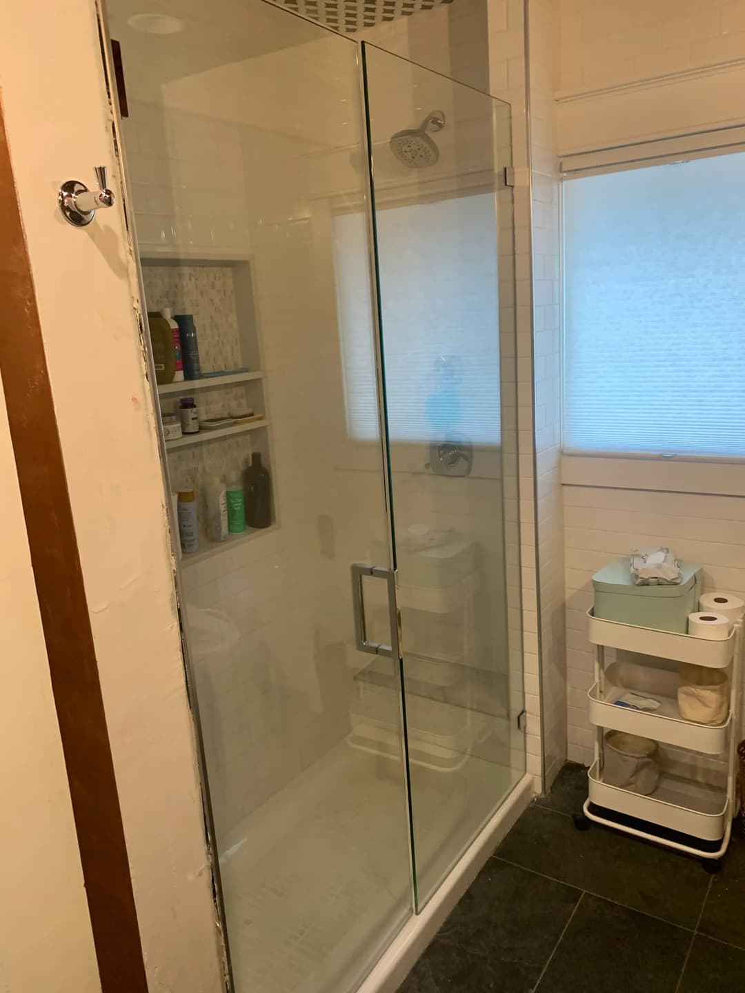 Modern glass shower enclosure with shelves and a towel cart in a bright bathroom setting.