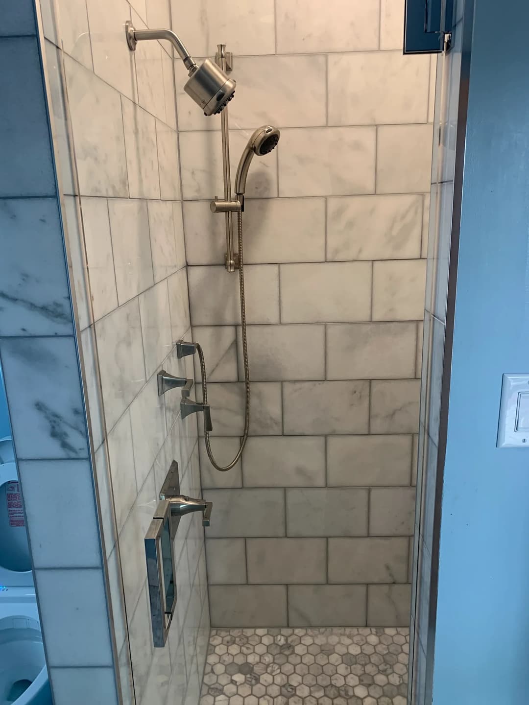 Modern shower with marble tiles, handheld showerhead, and sleek chrome fixtures.