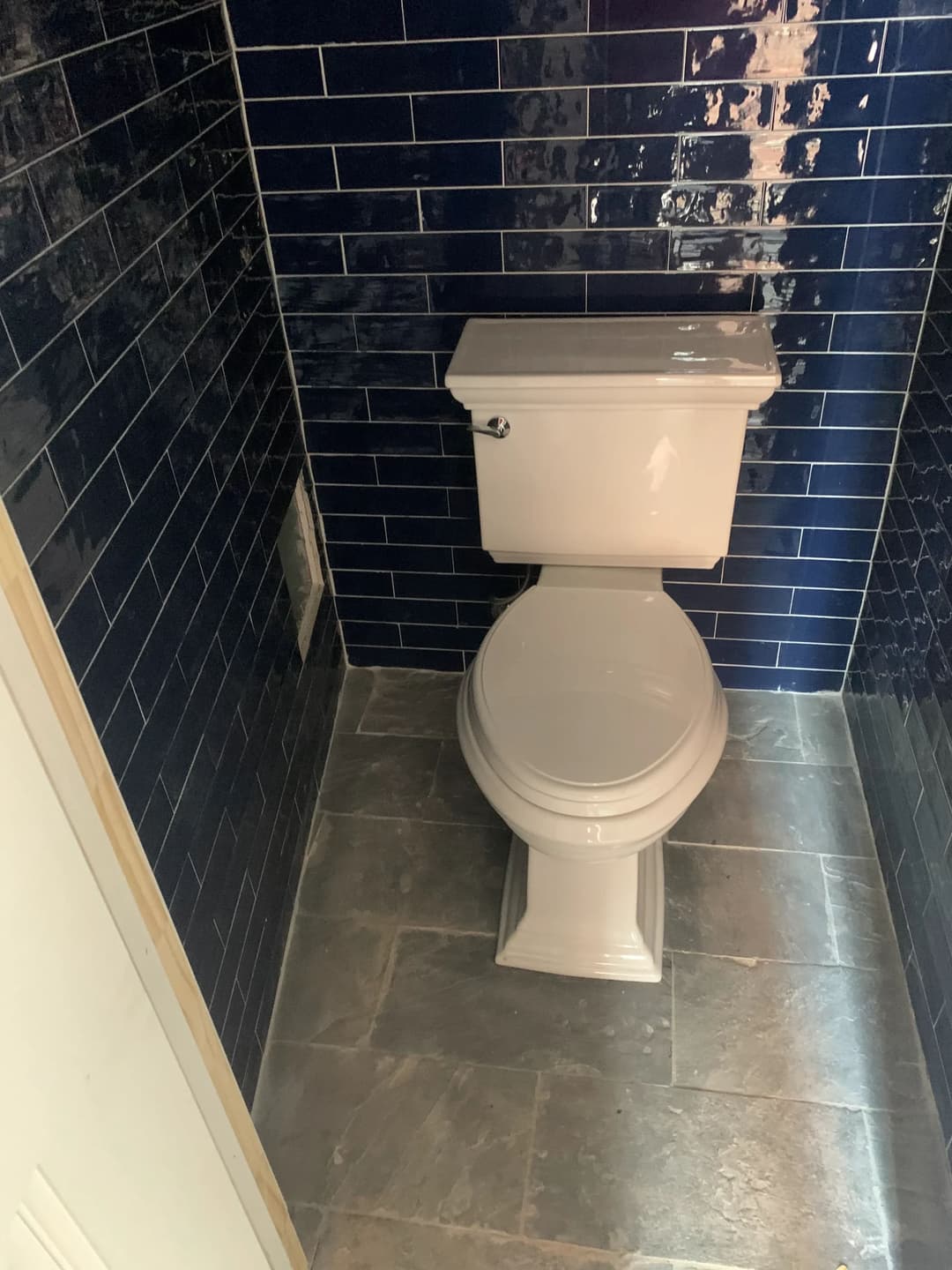 Modern white toilet in a bathroom with dark blue tiled walls and stone floor.