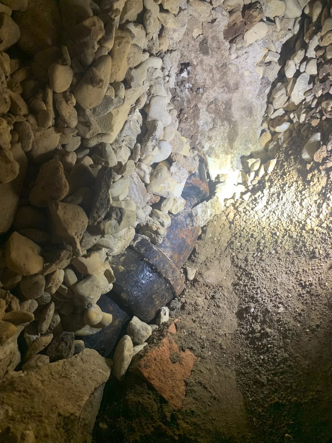 Hidden artifact among rocks and dirt in a dimly lit excavation site.