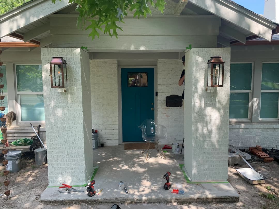 Front porch renovation with teal door, new lanterns, and tools on the ground.