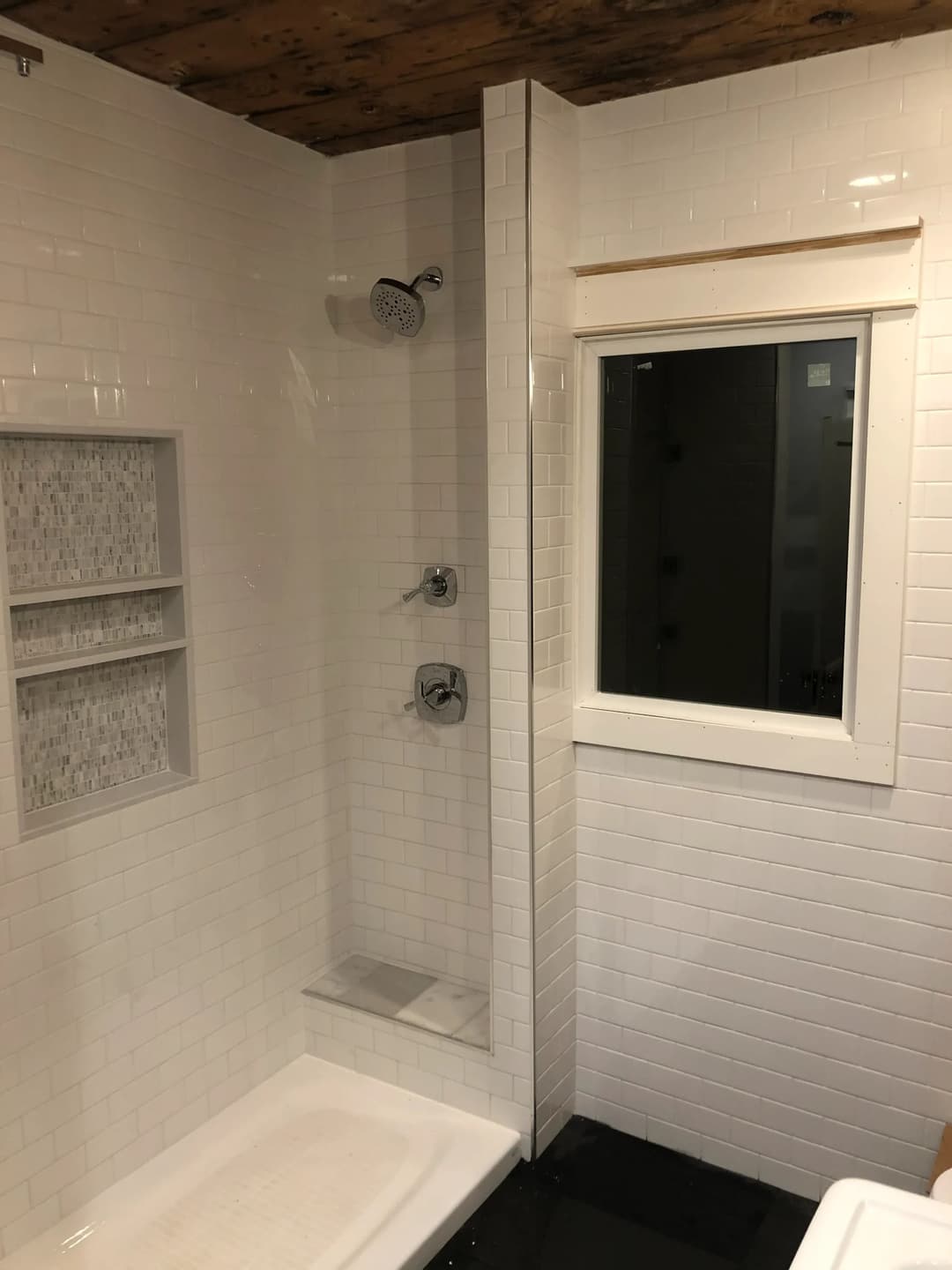 Modern bathroom with white tiled shower, shelf, and window. Elegant design with natural light.