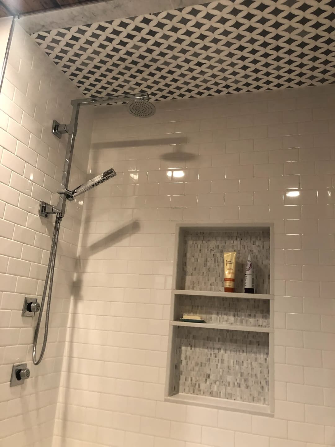 Modern shower with a rain showerhead, white tiles, and a built-in shelf for toiletries.