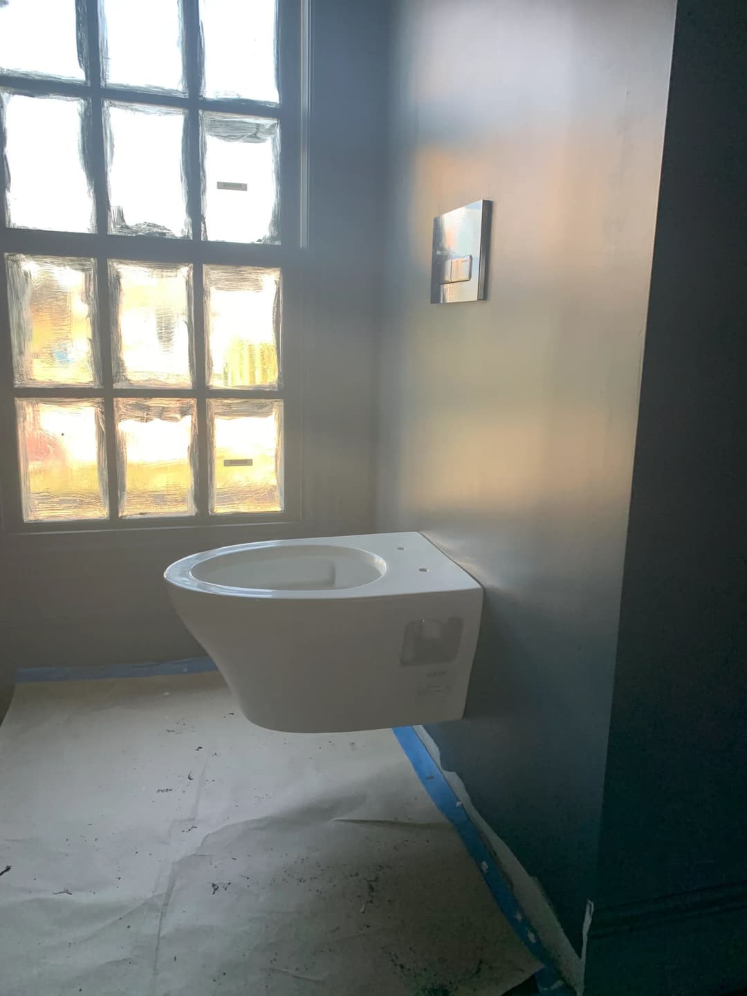 Modern wall-mounted toilet in a partially finished bathroom with a window.