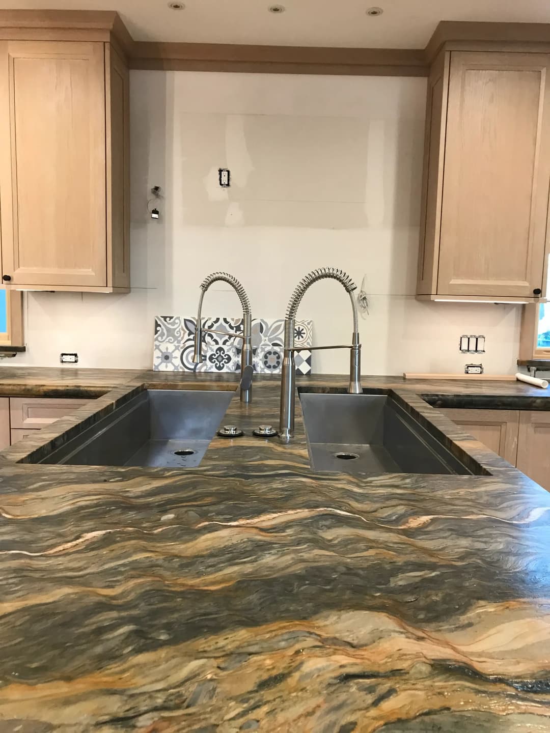 Modern kitchen with dual sinks, wood cabinetry, and colorful backsplash tile.