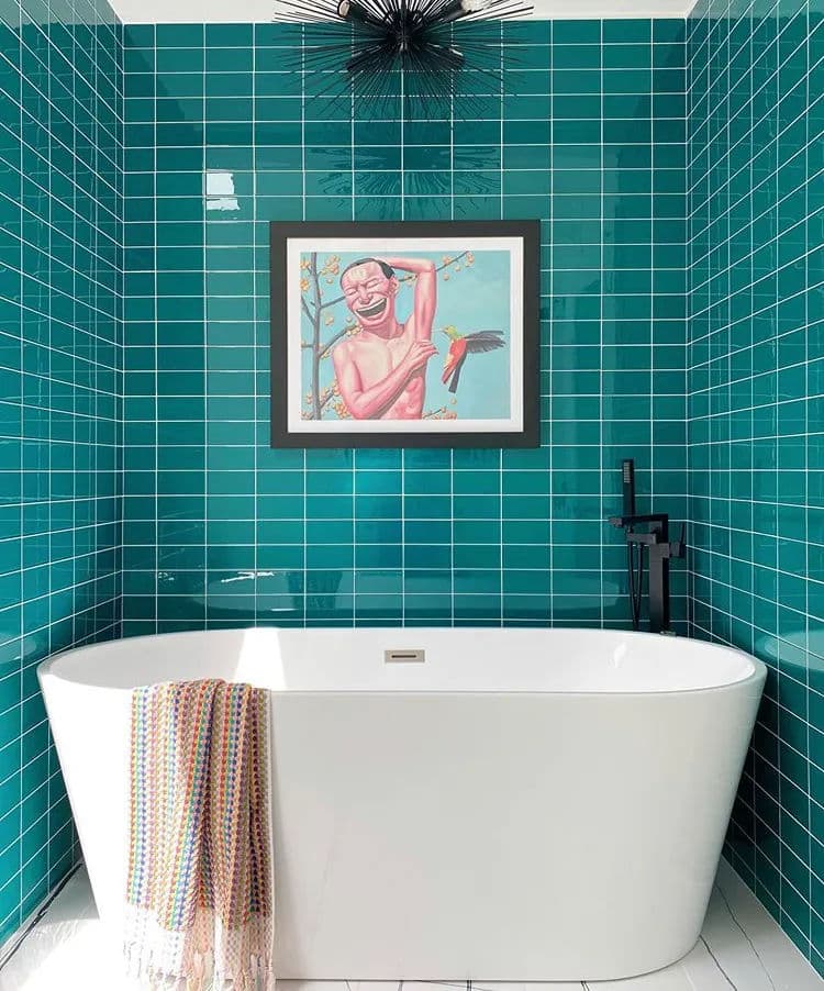 Modern bathroom with teal tiled walls, a freestanding bathtub, and vibrant artwork.