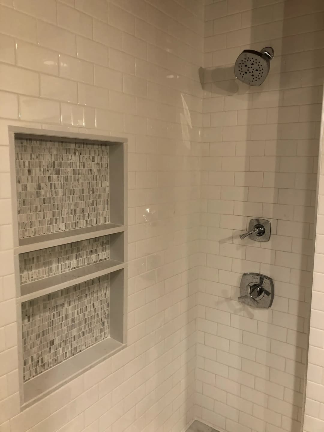 Modern shower with white tiles, rain showerhead, and recessed niche for toiletries.