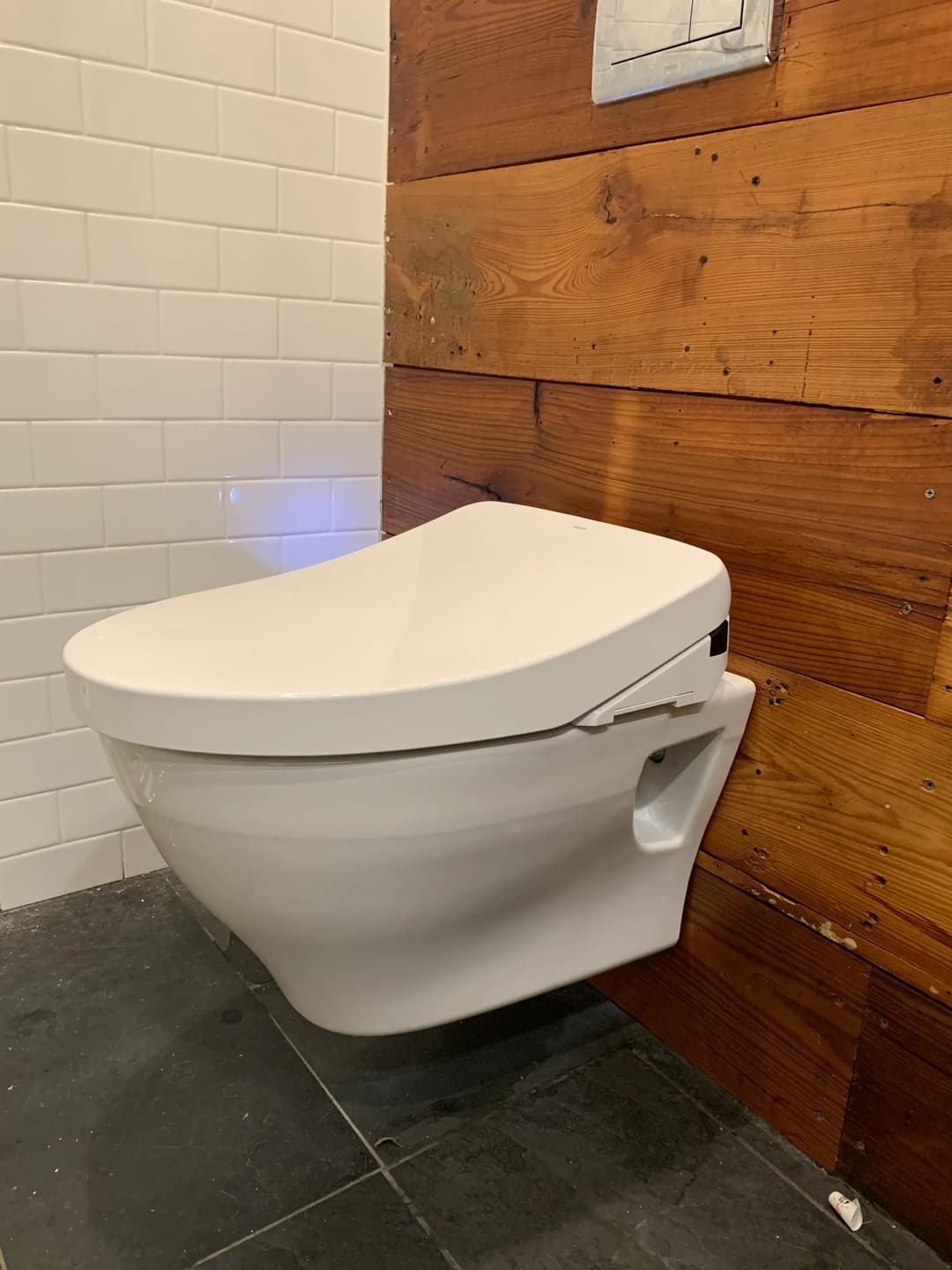 Modern wall-mounted toilet with wooden paneling in a contemporary bathroom setting.