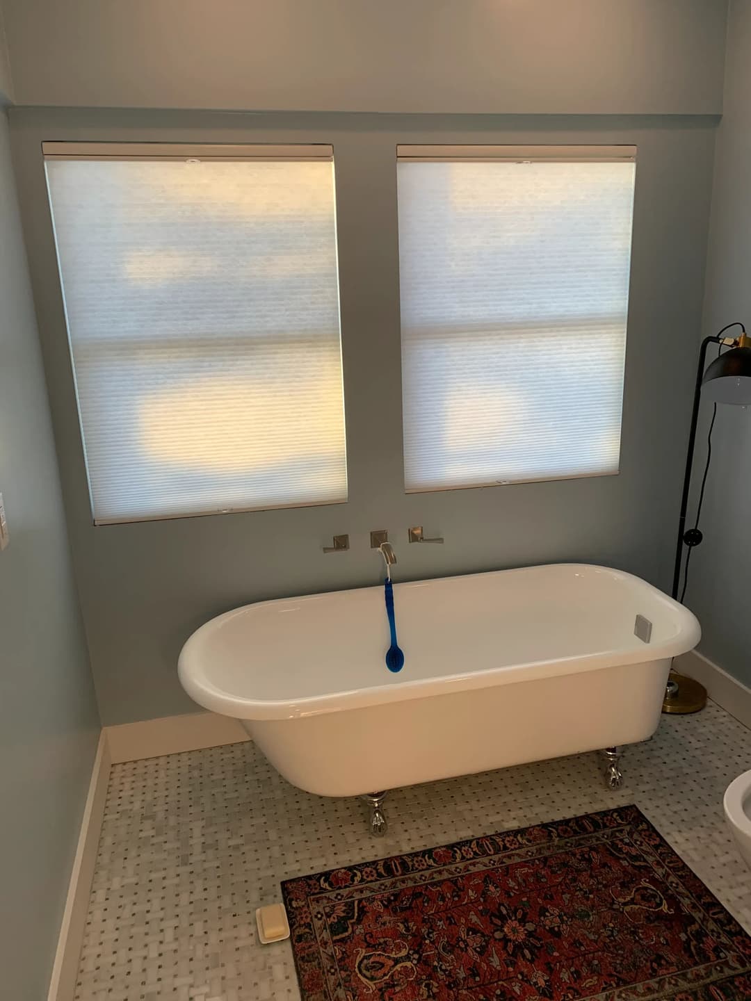 Modern bathroom featuring a freestanding bathtub, natural light from two windows, and a colorful rug.