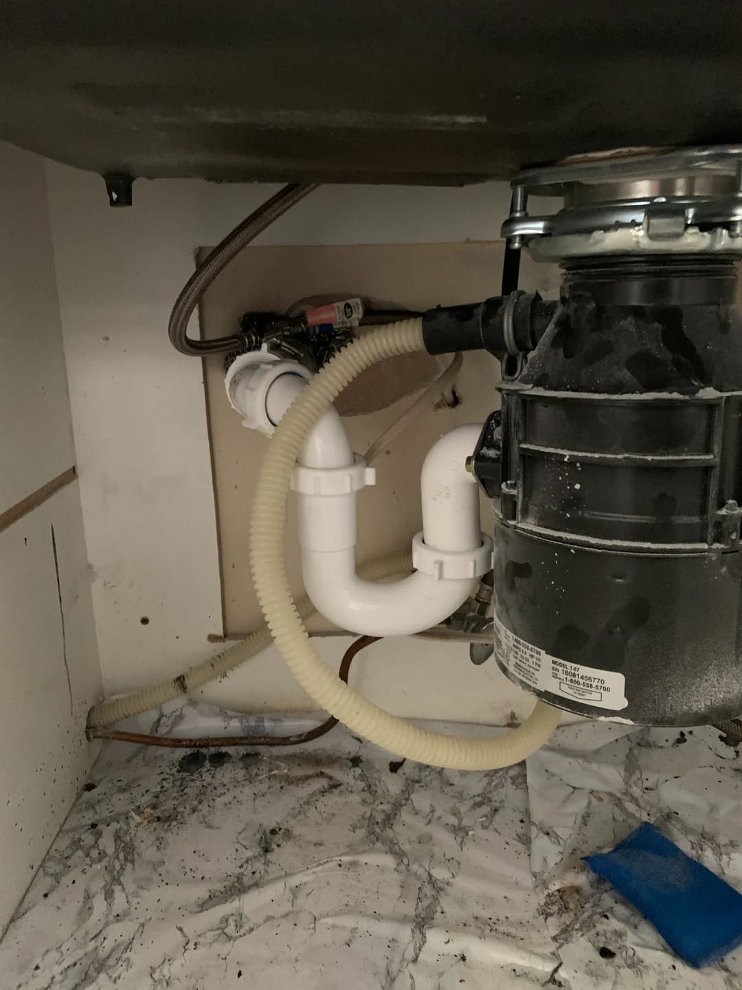 Under-sink garbage disposal with plumbing connections and visible wear on the surrounding area.