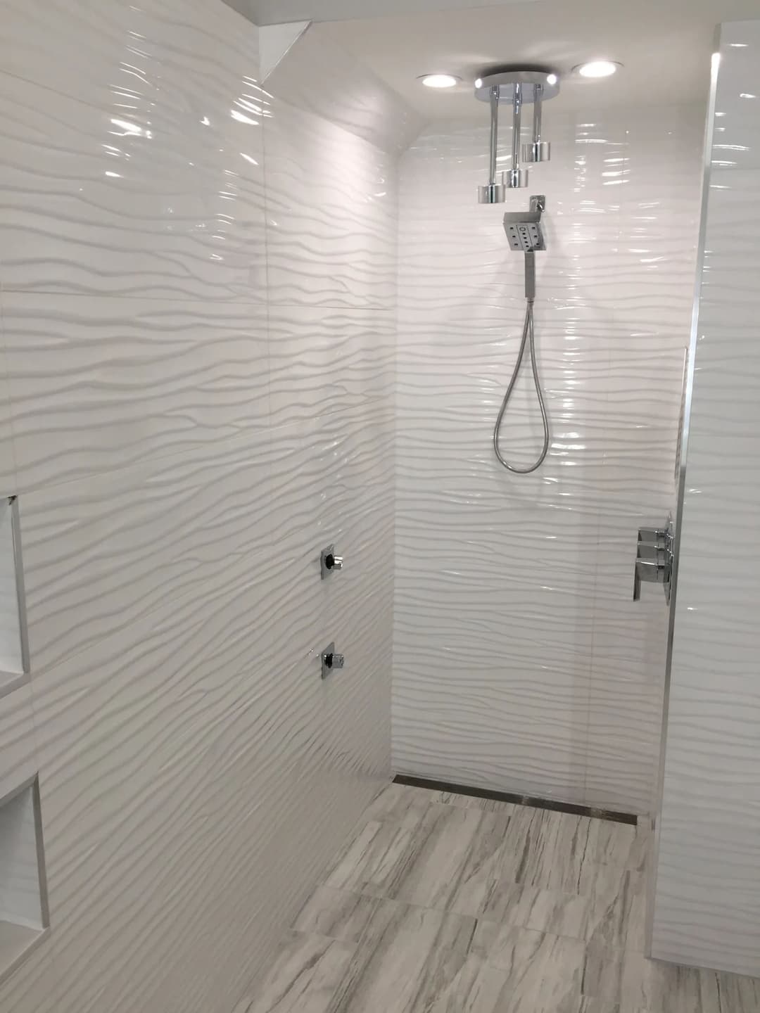 Modern shower with textured white tiles, overhead lighting, and sleek fixtures.