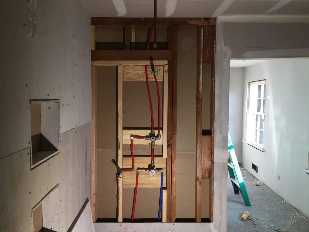 Framing of a bathroom wall with plumbing pipes and valves in a remodeled interior space.