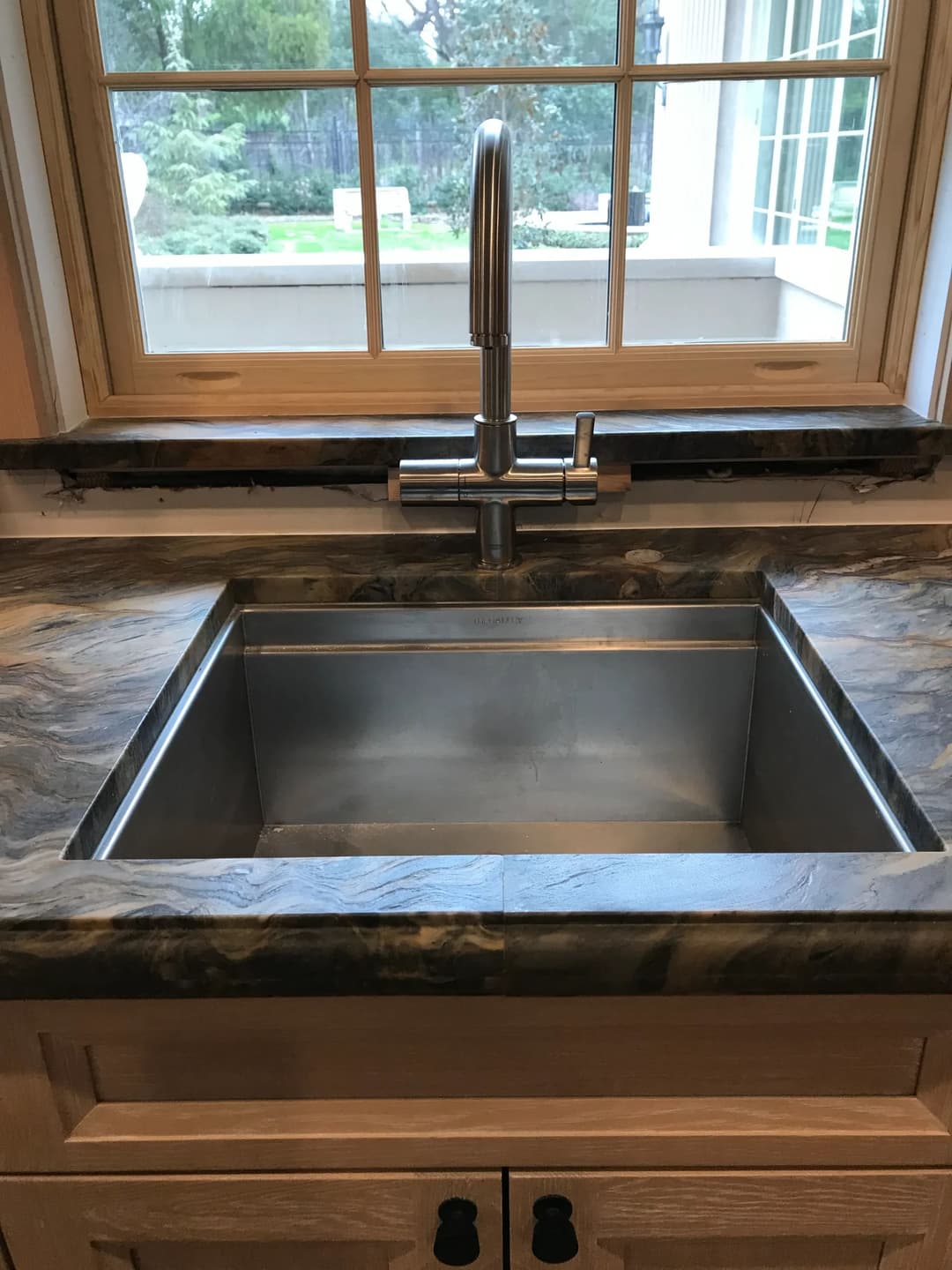 Stainless steel sink with modern faucet on a marble countertop near a bright window.