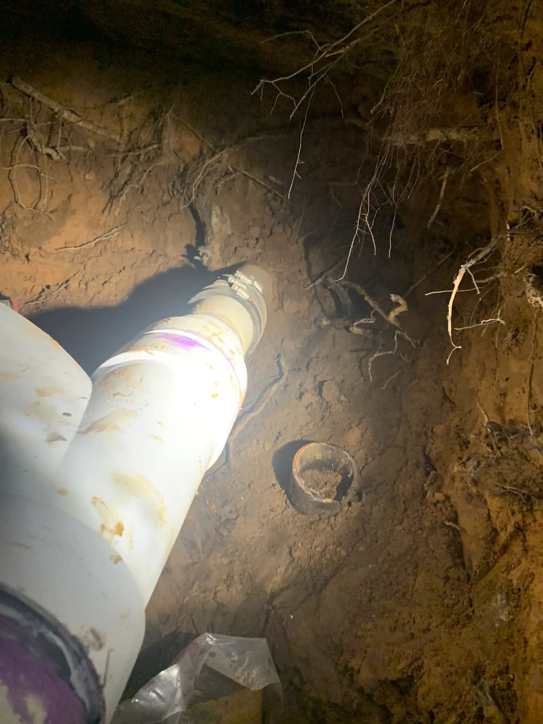 Underground pipe installation site with soil, roots, and dim lighting.