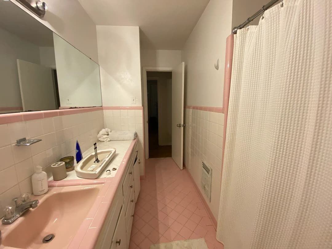 Bright pink-accented bathroom with a sink, mirror, shower curtain, and tiled flooring.