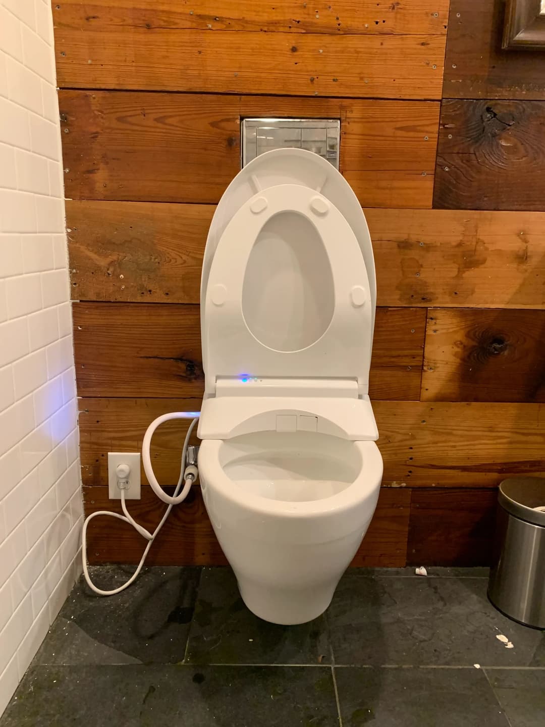 Modern toilet with wooden wall paneling and visible plumbing features.