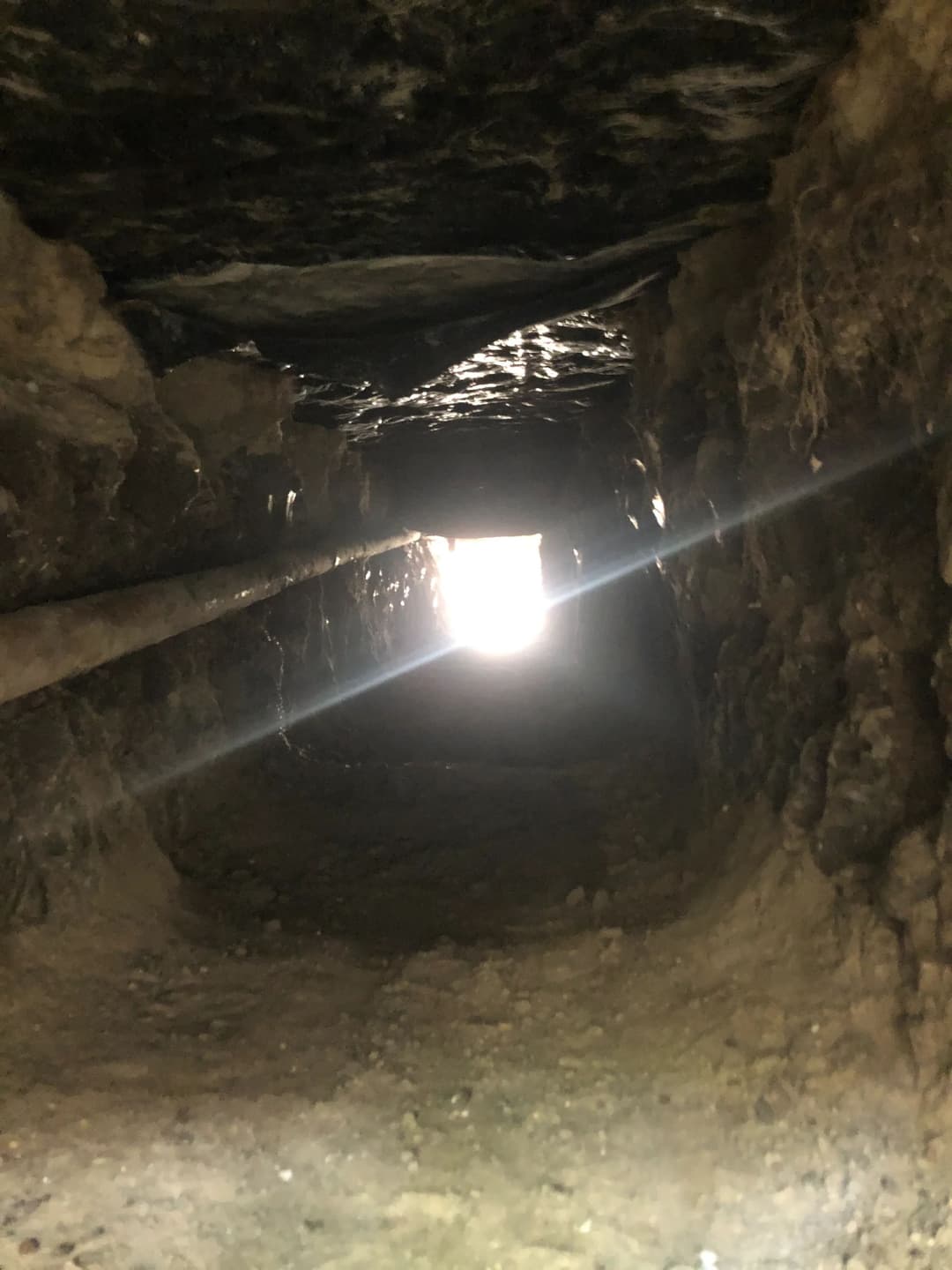 Light shining through a narrow tunnel, revealing rough, earthen walls.