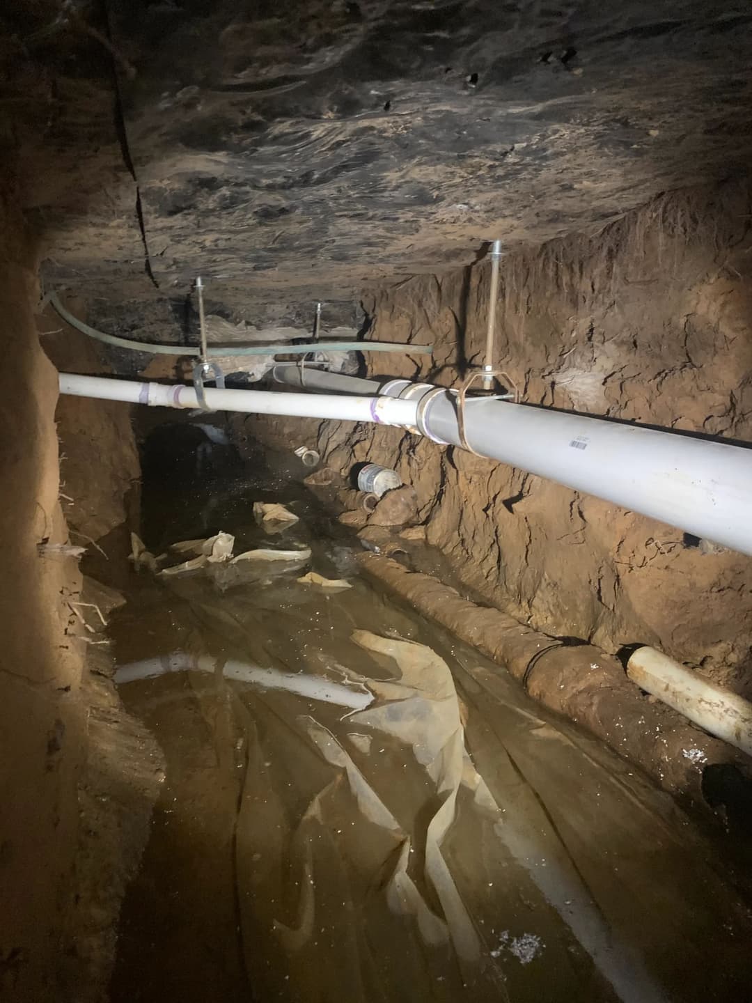 Underground tunnel with white pipes and water accumulation on the floor.