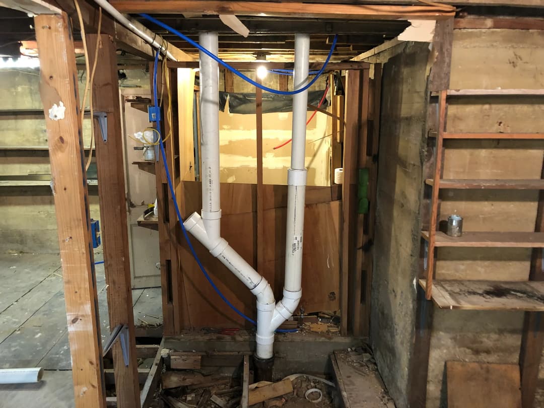 PVC plumbing pipes installed in a basement renovation, surrounded by wooden framework.