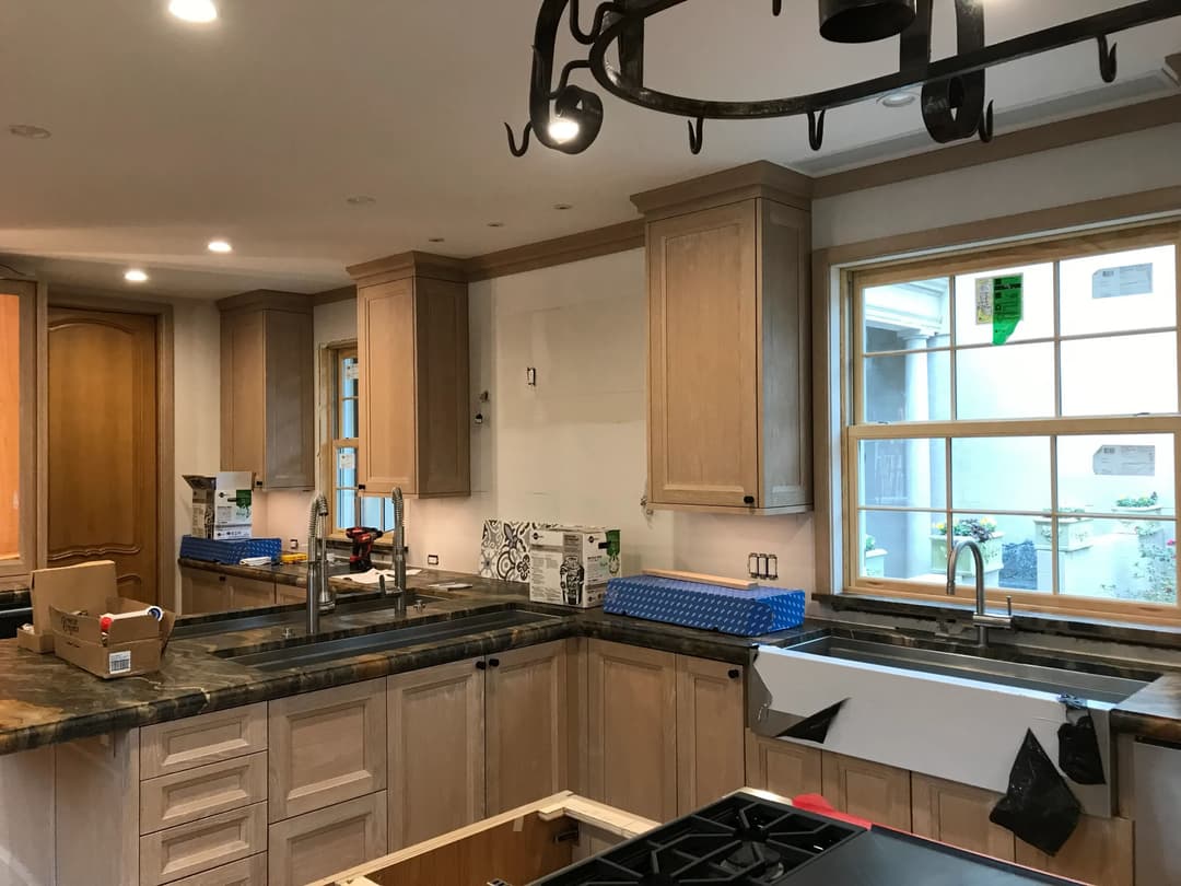 Modern kitchen under renovation with wooden cabinets and stone countertop. Bright natural light.