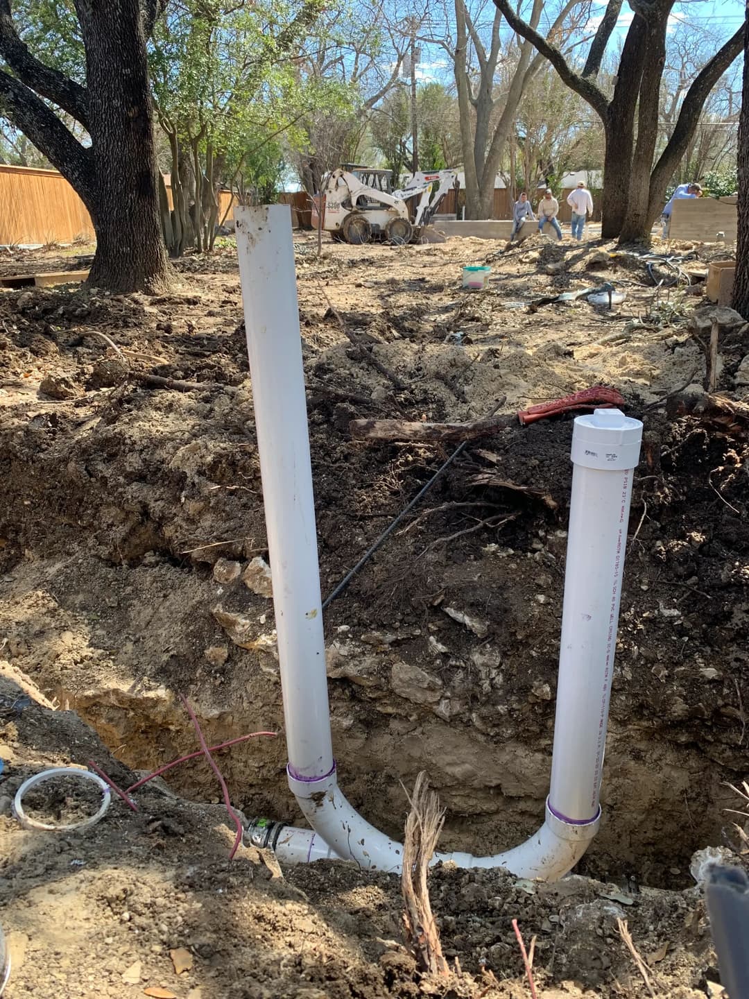 White PVC pipes emerging from a trench in a residential yard undergoing excavation.